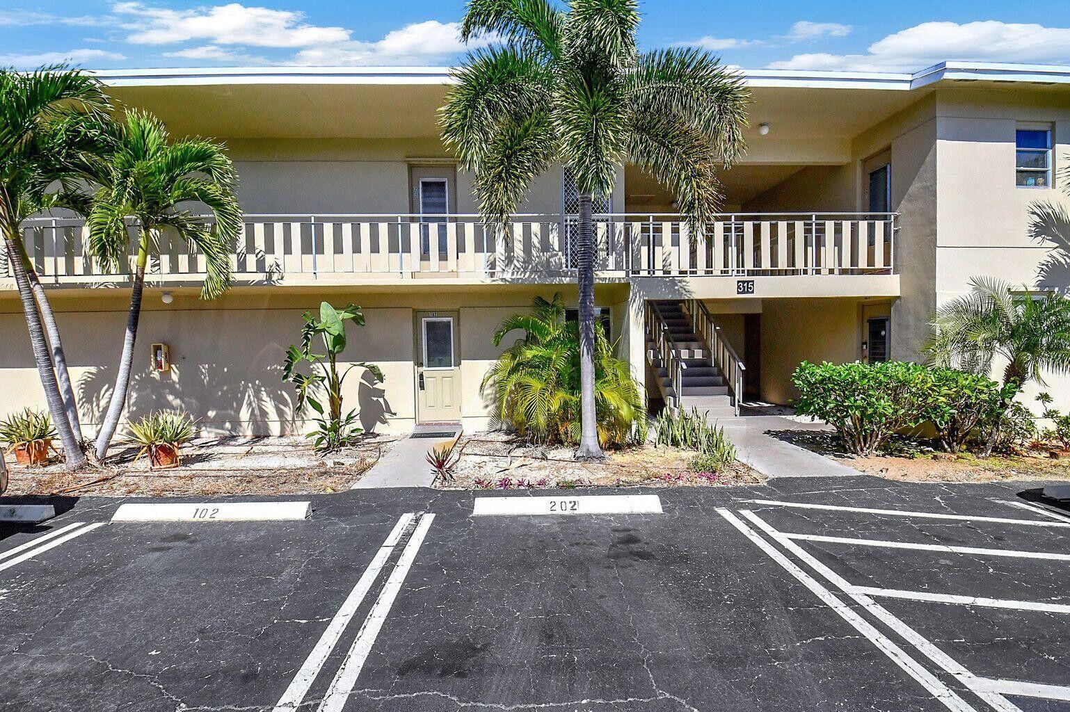 A two-story apartment building exterior features a parking lot, palm trees, and a staircase — 315 Circle Drive S # 102, Boynton Beach FL 33435, BOYNTON BEACH, FL