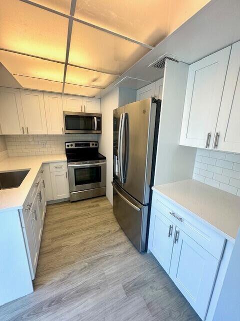 A modern kitchen features white cabinets, stainless steel appliances, and light wood-look flooring — 315 Circle Drive S # 102, Boynton Beach FL 33435, BOYNTON BEACH, FL