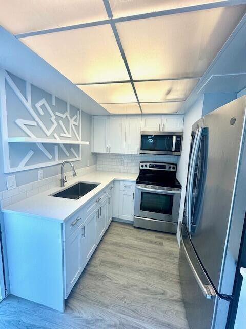 A modern kitchen features white cabinets, stainless steel appliances, and a geometric wall accent — 315 Circle Drive S # 102, Boynton Beach FL 33435, BOYNTON BEACH, FL