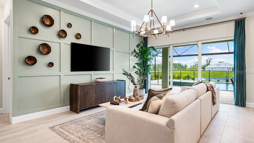A living room features a paneled sage green wall, a television, and a sliding glass door — 11235 CARDING MILL LANE, WINTER GARDEN, FL
