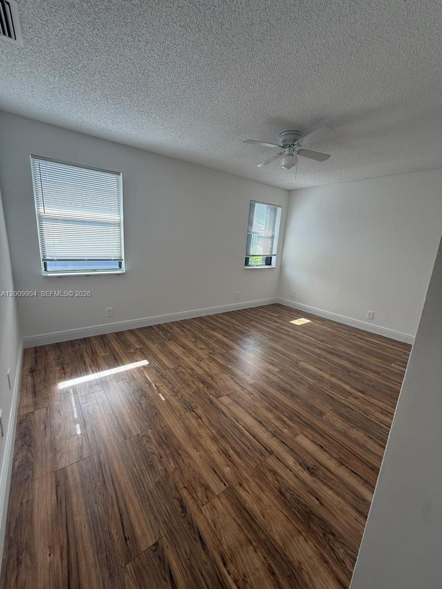 An empty bedroom features white walls, wood-look flooring, two windows with blinds, and a ceiling fan — 16413 Grape Way, Delray Beach FL 33484, DELRAY BEACH, FL