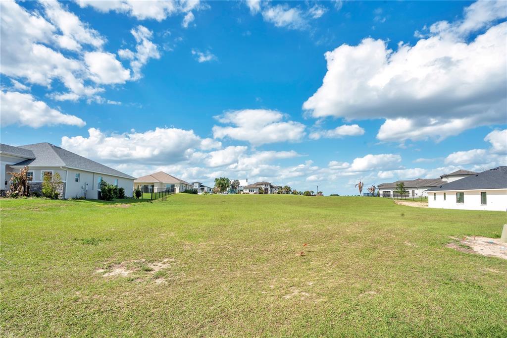 A vacant grassy lot is surrounded by residential houses under a bright blue sky — 228 SNOWY ORCHID WAY, LAKE ALFRED, FL