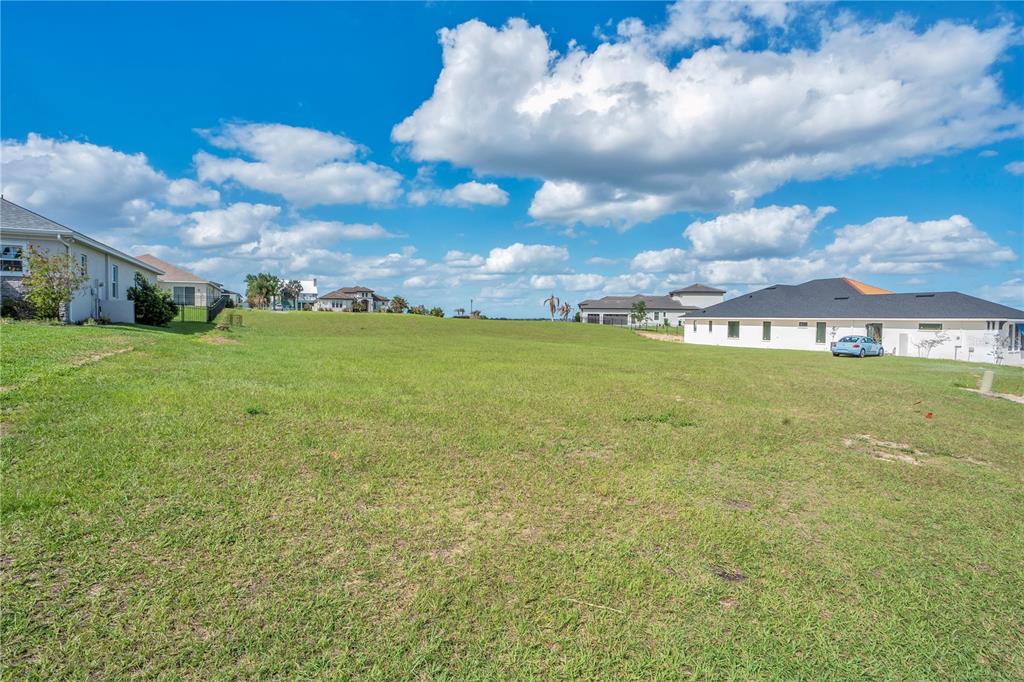 A large, grassy vacant lot is situated between several suburban houses under a cloudy sky — 228 SNOWY ORCHID WAY, LAKE ALFRED, FL
