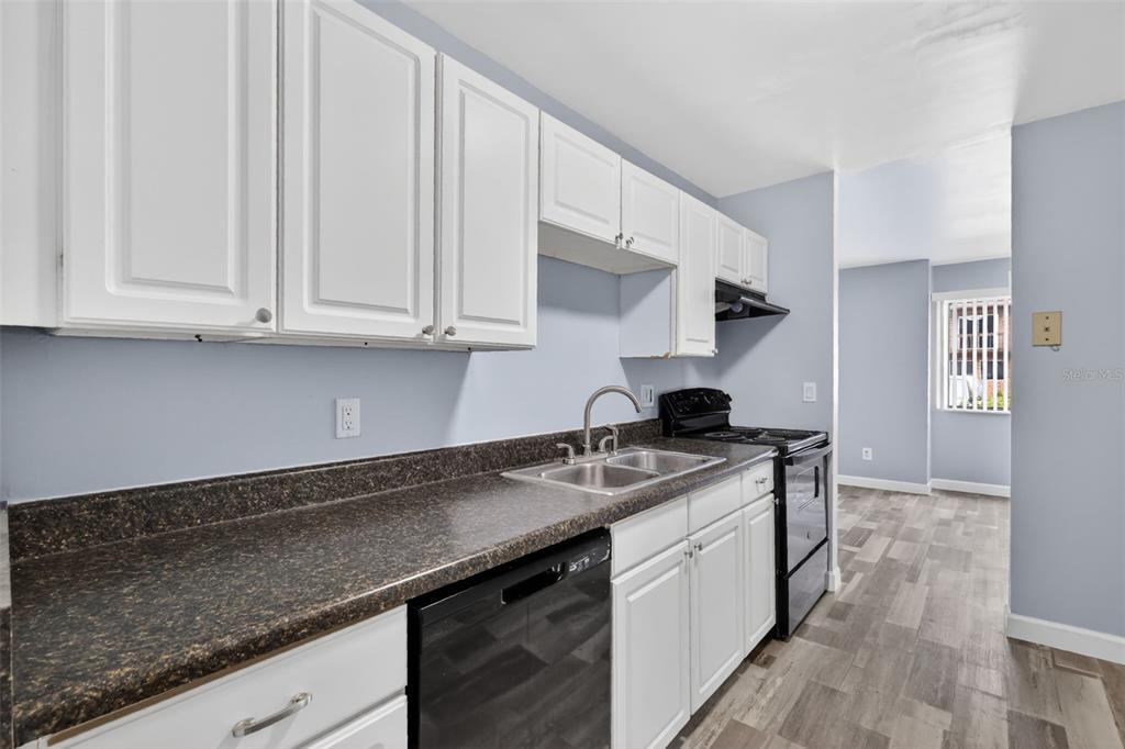 A kitchen features white cabinets, dark countertops, black appliances, and light wood-look flooring — 5121 PICADILLY CIRCUS COURT, ORLANDO, FL