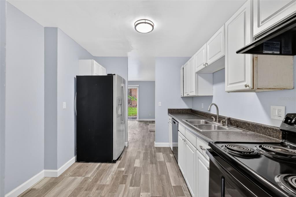 A kitchen with white cabinets, black appliances, dark countertops, and light wood-look flooring — 5121 PICADILLY CIRCUS COURT, ORLANDO, FL