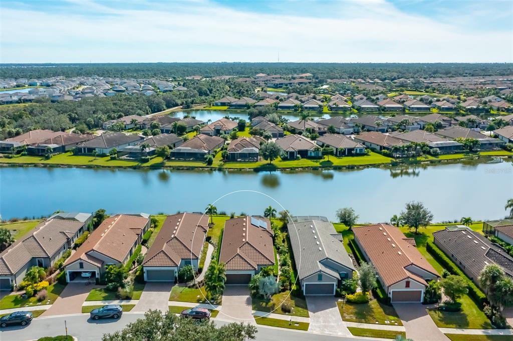 An aerial view shows a suburban neighborhood with houses bordering a lake — 5451 LAGO MAGGIO STREET, SARASOTA, FL