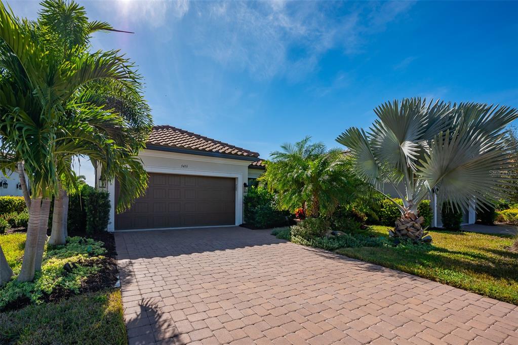 A single-story house with a brown garage door and a paved driveway surrounded by palm trees — 5451 LAGO MAGGIO STREET, SARASOTA, FL
