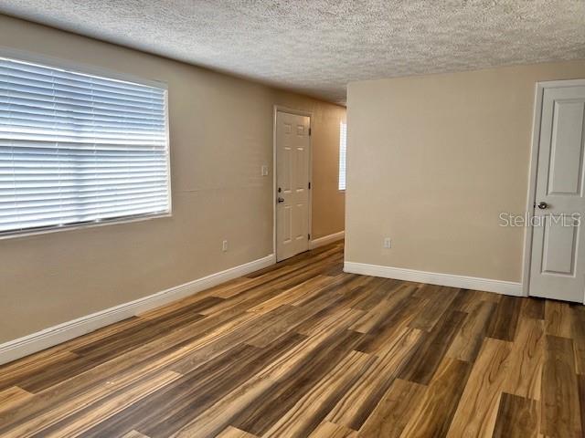 An empty room features wood-look flooring, beige walls, a window with blinds, and two doors — 6413 SUTTERS MILL ROAD, NEW PORT RICHEY, FL