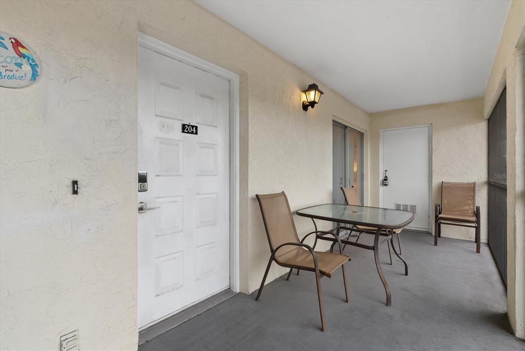 A covered balcony features a white door labeled 204, a glass-top table, and three chairs — 1531 PLACIDA ROAD UNIT 204, ENGLEWOOD, FL
