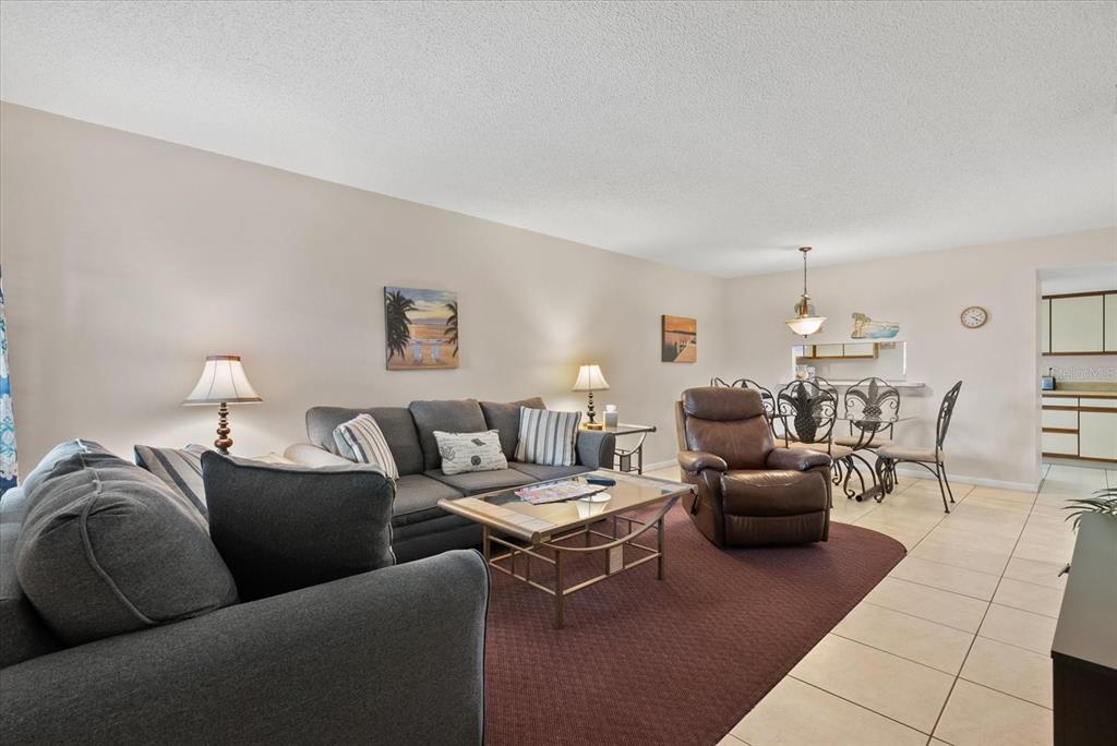 A living room with a gray sofa, brown recliner, glass coffee table, and dining area — 1531 PLACIDA ROAD UNIT 204, ENGLEWOOD, FL