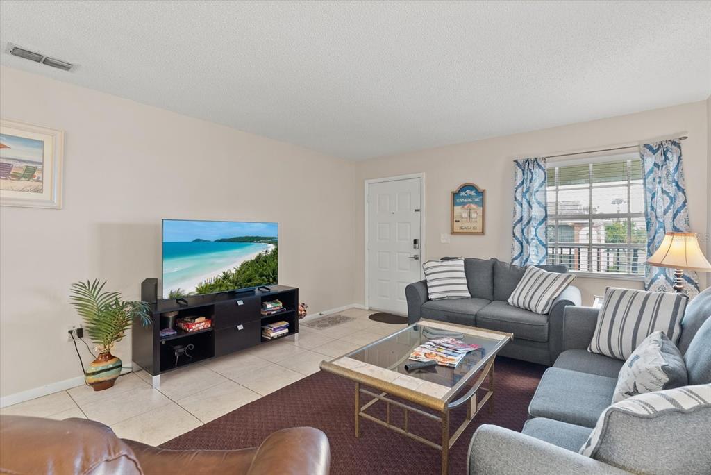 A living room features tile flooring, a dark area rug, a television, and gray sofas — 1531 PLACIDA ROAD UNIT 204, ENGLEWOOD, FL