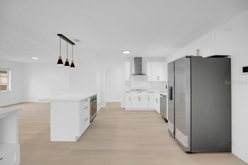 A modern kitchen features white cabinetry, a central island, stainless steel appliances, and light flooring — 1241 MANCHESTER ROAD, MAITLAND, FL