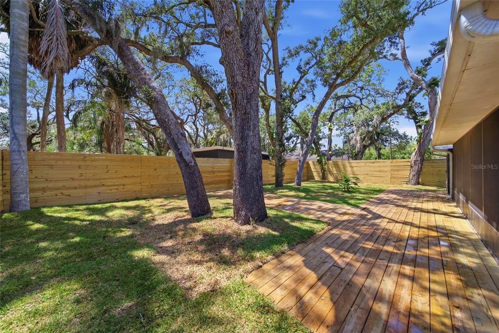 A wooden deck extends from a house into a backyard with large trees and fencing — 7247 OELSNER STREET, NEW PORT RICHEY, FL