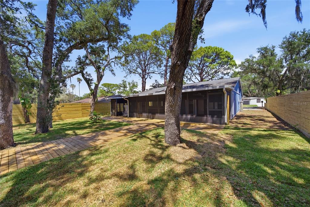 A backyard view of a house with a screened-in porch, wooden walkway, and wooden fences — 7247 OELSNER STREET, NEW PORT RICHEY, FL