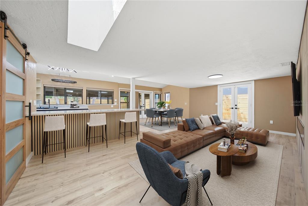 An open-concept living and dining area features a kitchen island, wood flooring, and modern furniture — 7247 OELSNER STREET, NEW PORT RICHEY, FL