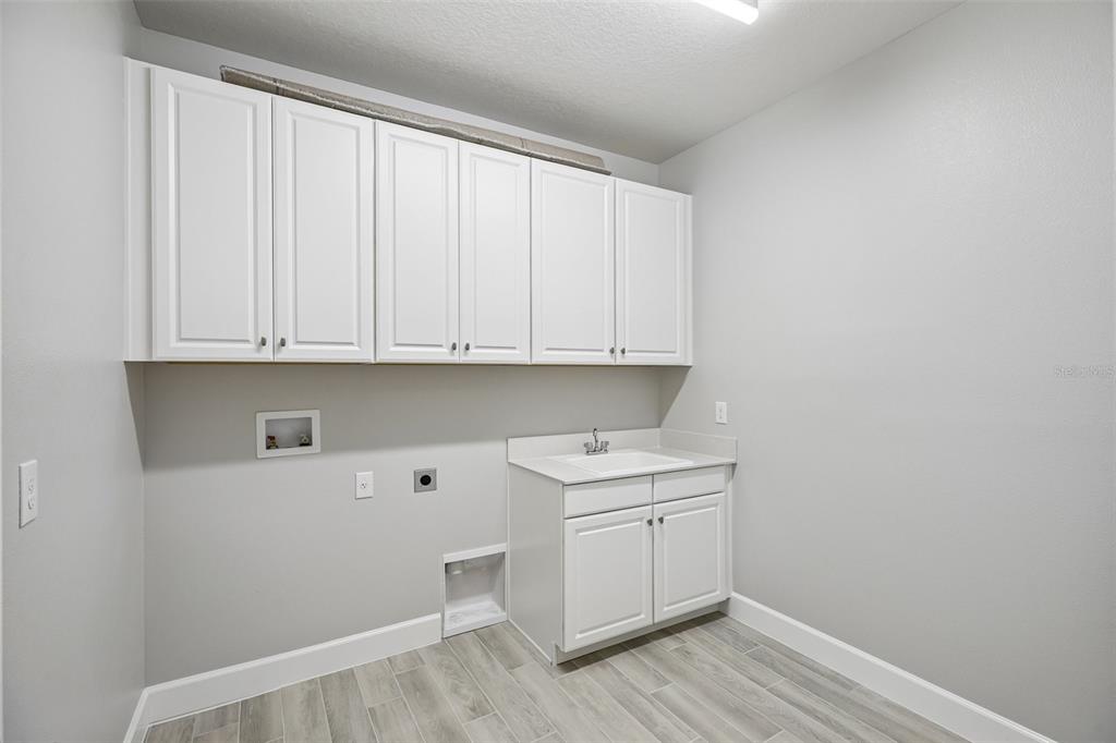 A laundry room features white cabinets, a utility sink, and light gray wood-look tile flooring — 3233 WOLF LAKE AVENUE, APOPKA, FL
