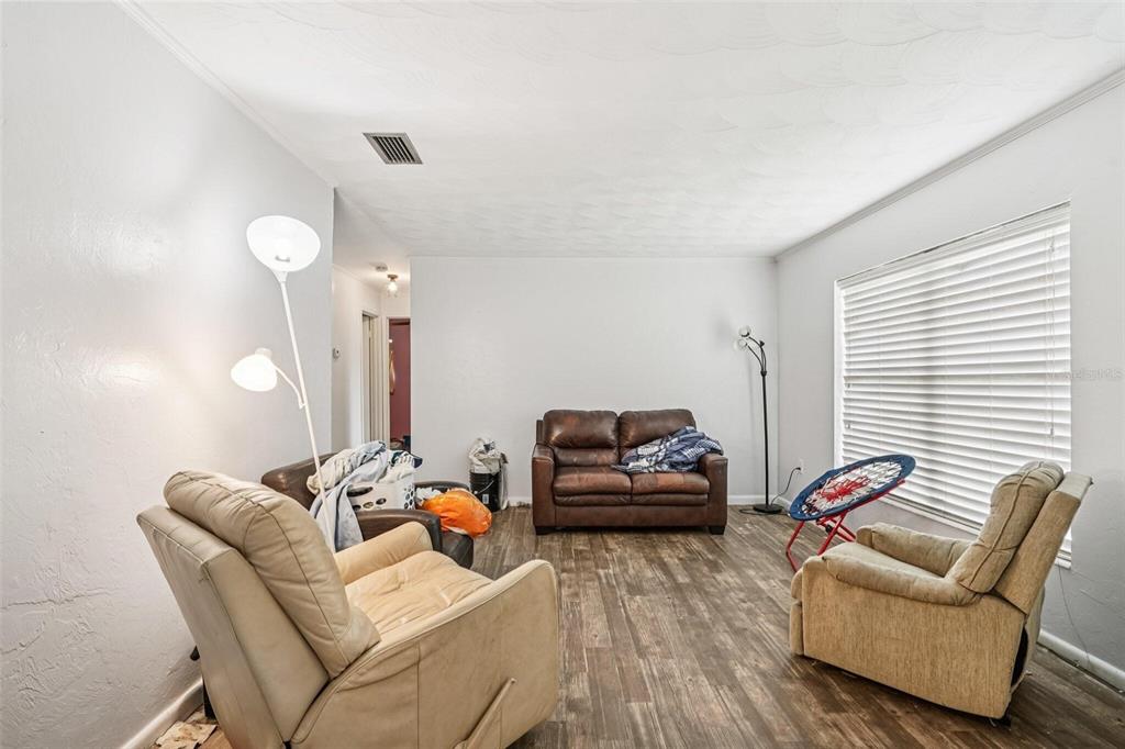 A living room features wood-look flooring, white walls, a brown sofa, and two beige recliners — 15019 NW 134TH TERRACE, ALACHUA, FL