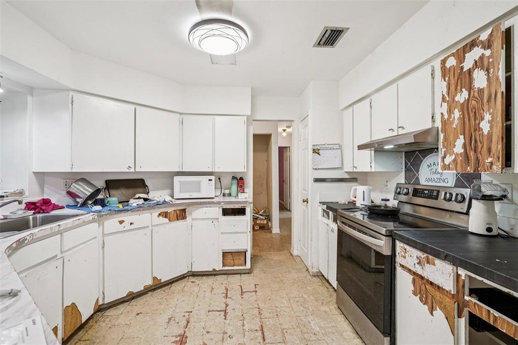 A kitchen with white cabinets showing significant wear, a stainless steel stove, and tiled flooring — 15019 NW 134TH TERRACE, ALACHUA, FL