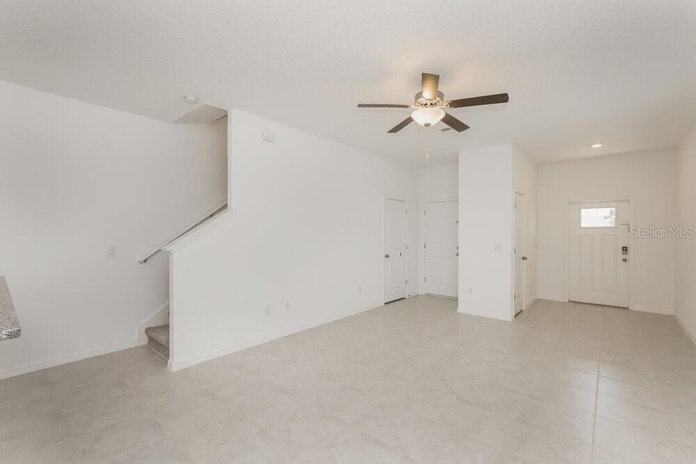 A bright, open-concept living area features white walls, light tile flooring, and a staircase — 2136 AZURE VIEW WAY, LUTZ, FL