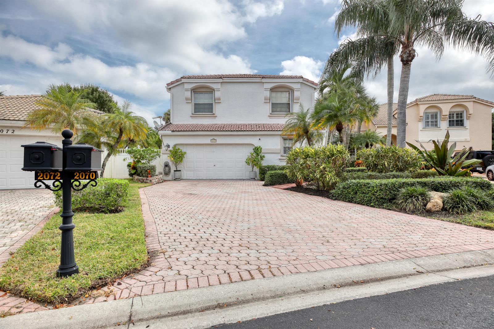 A two-story white stucco house features a paved driveway, a two-car garage, and palm trees — 2070 Chagall Circle, West Palm Beach FL 33409, WEST PALM BEACH, FL