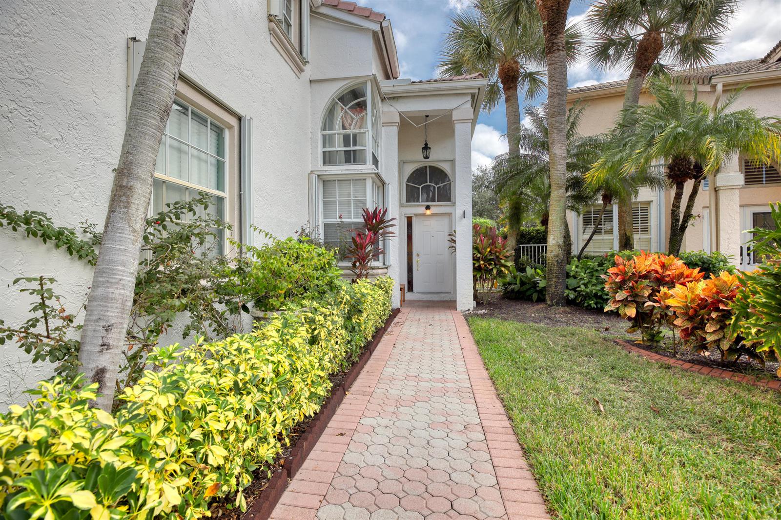 A paved walkway leads to the white front door of a house with palm trees — 2070 Chagall Circle, West Palm Beach FL 33409, WEST PALM BEACH, FL