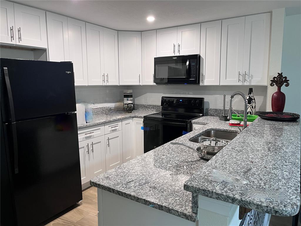 A kitchen features white cabinets, granite countertops, and black appliances — 1147 E MCDONALD AVENUE UNIT 202, EUSTIS, FL