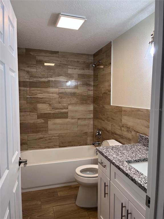 A bathroom features a wood-look tile tub surround, a white vanity with granite, and a toilet — 1147 E MCDONALD AVENUE UNIT 202, EUSTIS, FL