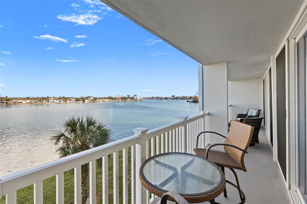 A balcony with a glass-topped table and chairs overlooks a wide body of water — 500 TREASURE ISLAND CAUSEWAY UNIT 308, TREASURE ISLAND, FL