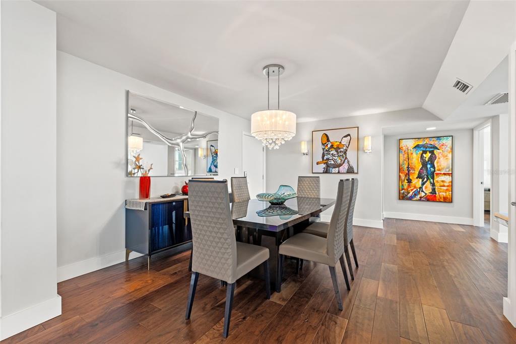 A dining room features a dark table, grey chairs, a chandelier, and colorful wall art — 500 TREASURE ISLAND CAUSEWAY UNIT 308, TREASURE ISLAND, FL