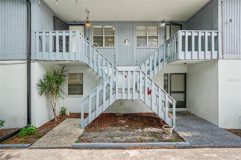 An exterior view of a two-story apartment building with an outdoor staircase and wooden railings — 9208 N CONNECHUSETT ROAD UNIT C, TAMPA, FL