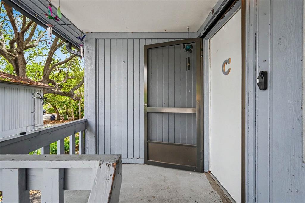 A gray wooden balcony features a screen door leading to an apartment entrance marked C — 9208 N CONNECHUSETT ROAD UNIT C, TAMPA, FL