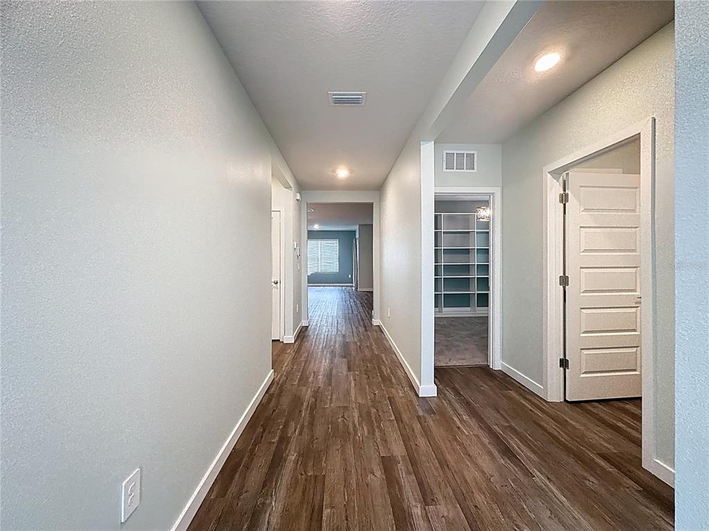 A hallway with wood-look flooring leads to an open room with built-in shelving — 3707 HATCHERY WAY, BRADENTON, FL