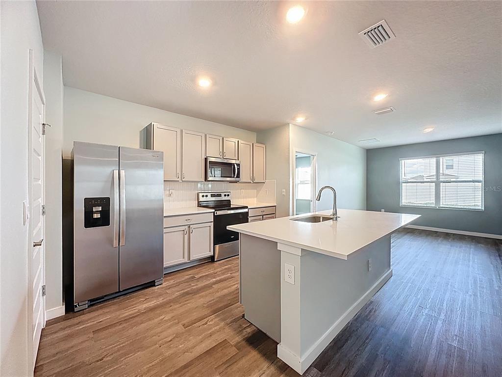 A kitchen with stainless steel appliances, white cabinets, a center island, and wood-look flooring — 3707 HATCHERY WAY, BRADENTON, FL