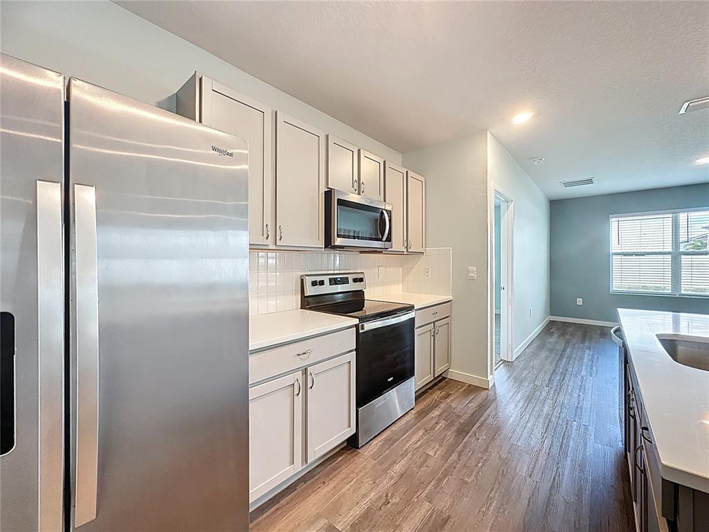A kitchen features stainless steel appliances, white cabinetry, and light countertops over wood-look flooring — 3707 HATCHERY WAY, BRADENTON, FL