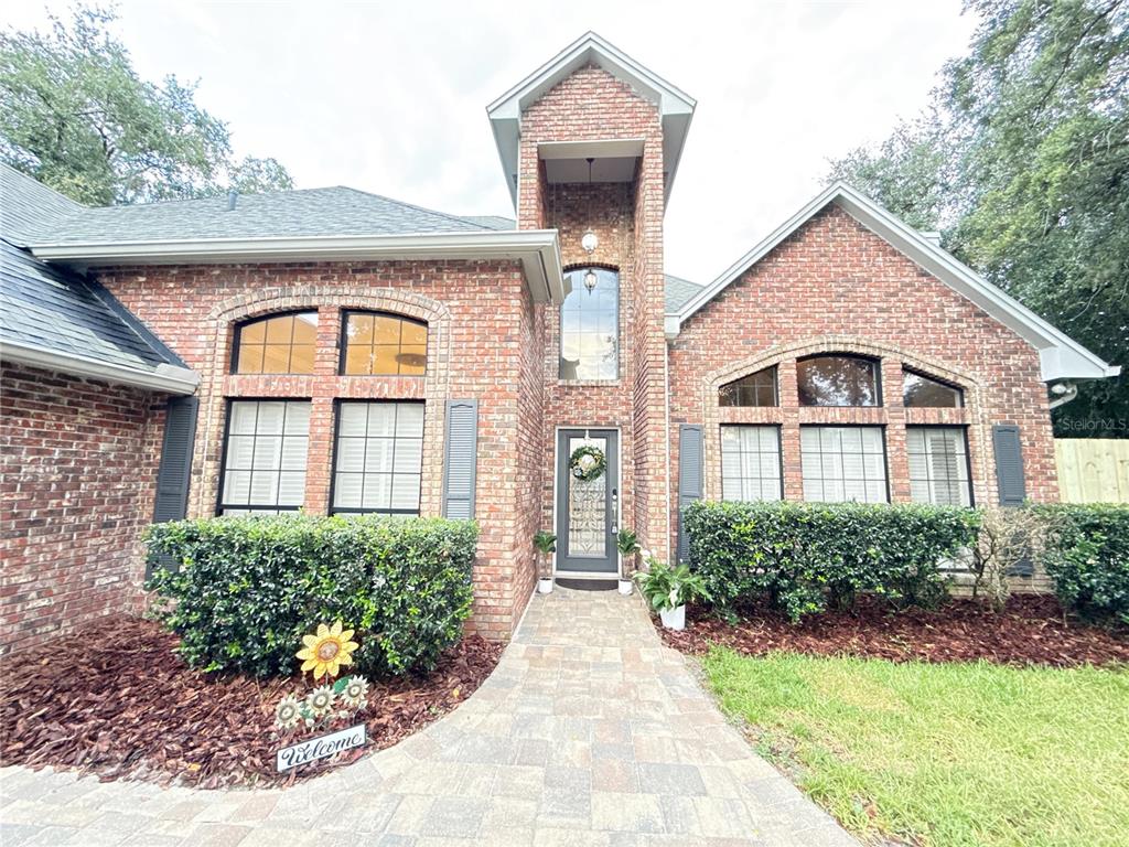 A brick house exterior features a central tower entrance, arched windows, and a paved walkway — 9918 BAY VISTA ESTATES BOULEVARD, ORLANDO, FL