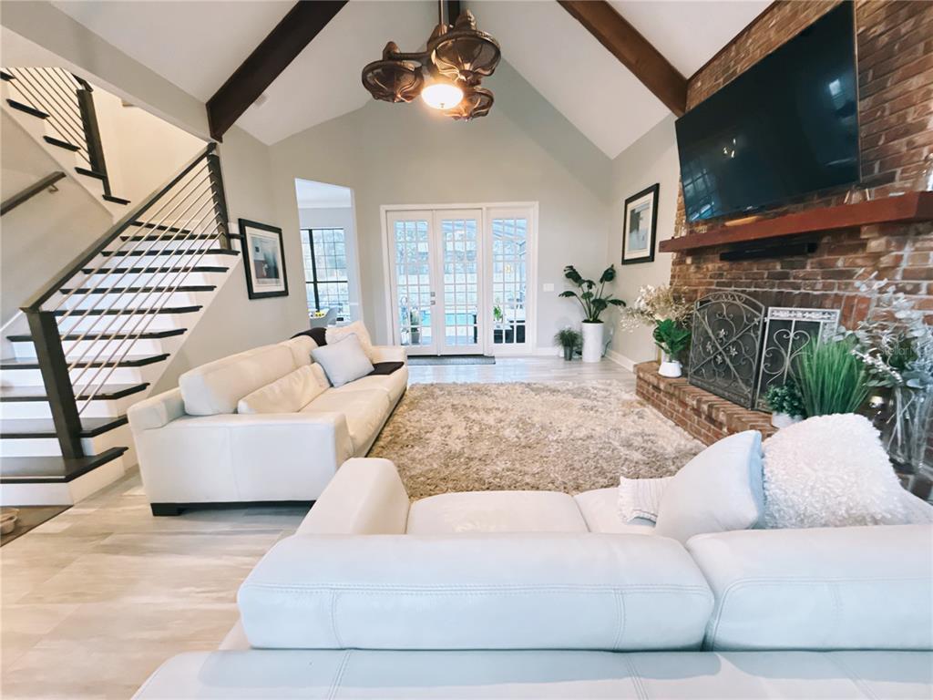 A living room features a vaulted ceiling, brick fireplace, white sofas, and a staircase — 9918 BAY VISTA ESTATES BOULEVARD, ORLANDO, FL