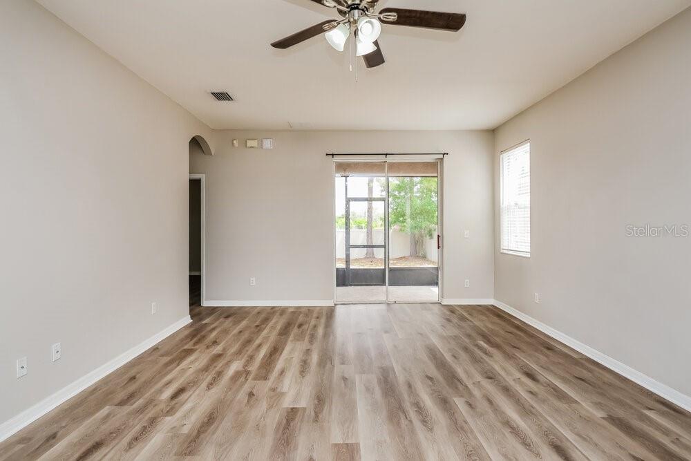 An empty living room features light-colored walls, wood-look flooring, and a sliding glass door — 908 LARWOOD PINE DRIVE, RUSKIN, FL