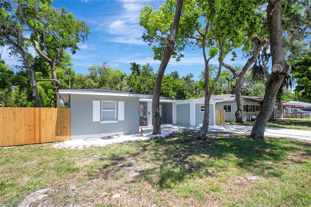 A gray single-story house with white shutters and a wooden fence stands among large trees — 6105 N 23RD STREET, TAMPA, FL