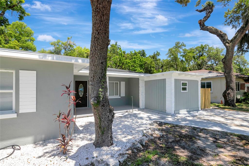 A gray, single-story house with a white-trimmed porch, gravel yard, and large trees — 6105 N 23RD STREET, TAMPA, FL
