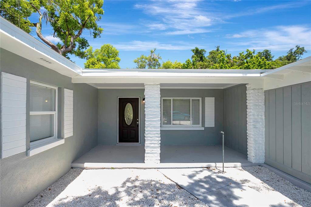 A gray house exterior features a covered porch with white stone pillars and a front door — 6105 N 23RD STREET, TAMPA, FL