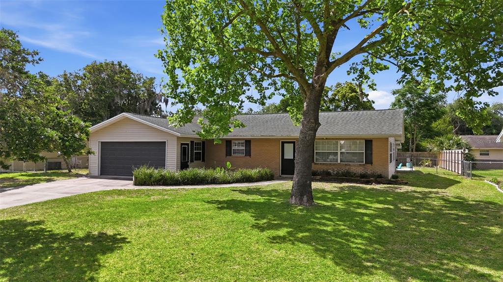 A single-story brick house with a garage, a large front tree, and a grassy lawn — 3996 LAKE ELEANOR DR, MOUNT DORA, FL