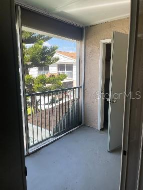 A screened-in balcony with a metal railing overlooks a residential area next to an open door — 7210 N MANHATTAN AVENUE UNIT 621, TAMPA, FL