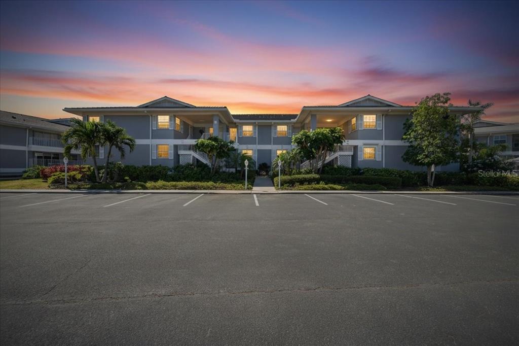 A two-story apartment building with a parking lot in the foreground at sunset — 1343 PERICO POINT CIRCLE UNIT 117, BRADENTON, FL