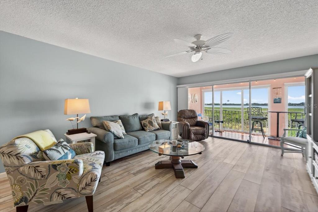 A living room with a sofa, patterned armchair, wood-look flooring, and a sliding glass door — 1343 PERICO POINT CIRCLE UNIT 117, BRADENTON, FL