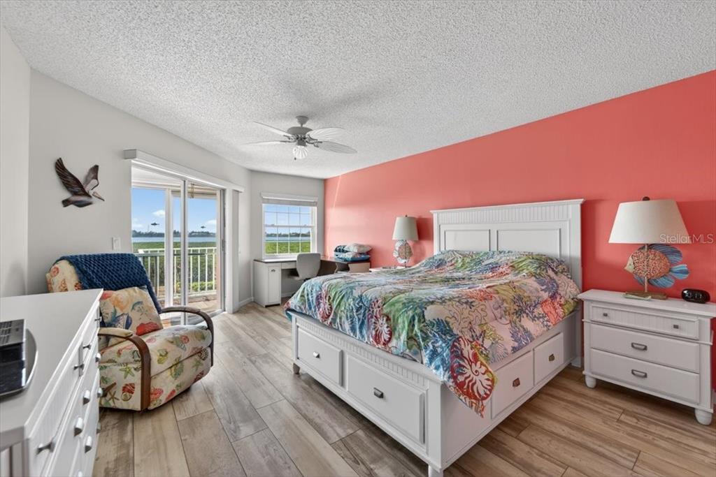 A bedroom features a coral accent wall, white furniture, a patterned bedspread, and a balcony — 1343 PERICO POINT CIRCLE UNIT 117, BRADENTON, FL