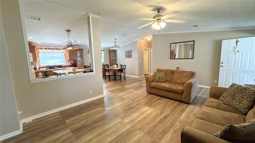 A living room with wood-look tile flooring opens into a dining area and kitchen — 1503 ALBY DRIVE lot 70, APOPKA, FL