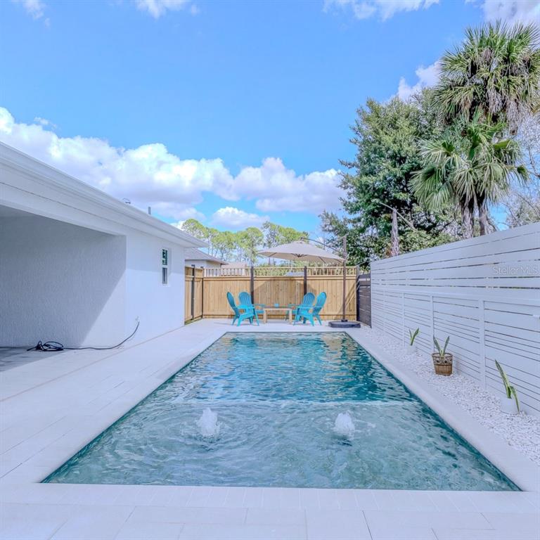 A rectangular swimming pool with fountains sits in a backyard patio area with blue chairs — 4638 CLARKE STREET, NORTH PORT, FL