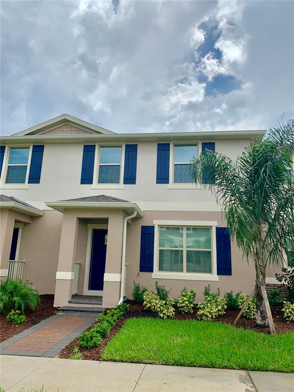 A two-story townhouse with beige stucco siding, blue shutters, and a brick walkway — 10094 TAWNY MEADOW ALLEY, WINTER GARDEN, FL
