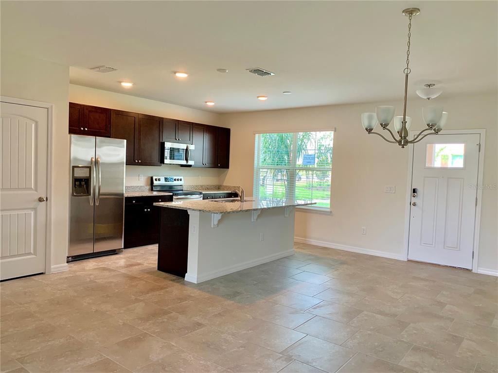 A kitchen features dark wood cabinets, granite countertops, a center island, and stainless steel appliances — 10094 TAWNY MEADOW ALLEY, WINTER GARDEN, FL