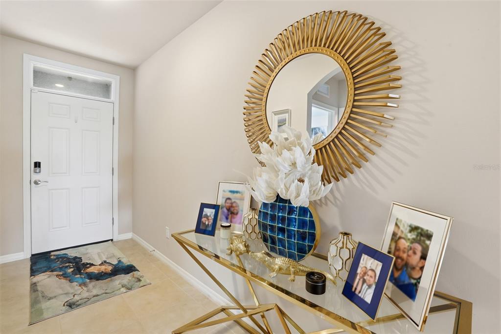 An entryway features a gold sunburst mirror, a glass console table, and a white door — 8909 CASCADE PRICE CIRCLE, NORTH FORT MYERS, FL